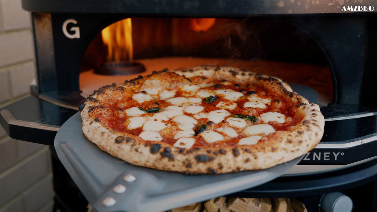 Gebackene Pizza mit Tomatensauce, hellem Käse und Basilikum auf dem Schieber vor einem Pizzaofen