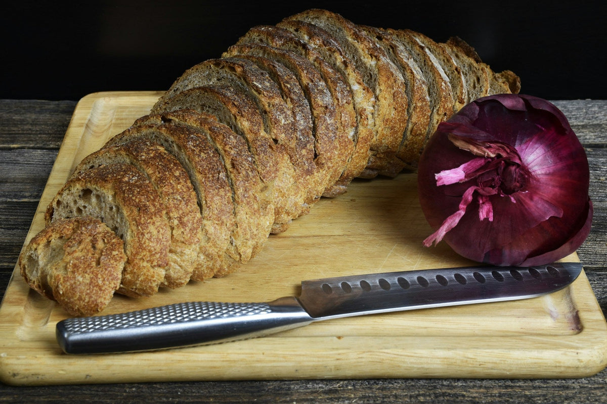 Stockfoto: in Scheiben geschnittener Brotlaib neben einer roten Zwiebel auf einem Holzbrett. Foto: Gennady Zakharin / Unsplash.