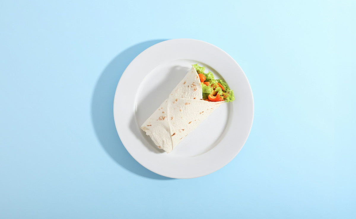 Stockfoto: Tortilla-Wrap mit Salat und sichtbarer Gemüsefüllung auf einem weißen Teller. Foto: Giorgio Trovato / Unsplash.