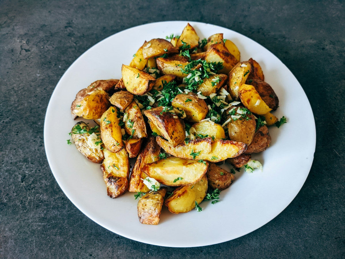 Stockfoto: goldbraun gebratene Kartoffelstücke mit Petersilie auf einem weißen Teller. Foto: Markus Winkler / Unsplash.