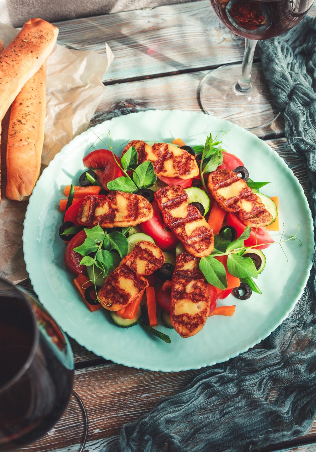 Stockfoto: gebräunte Halloumischeiben auf Salat mit Gurke, Tomaten, Paprika und Oliven. Foto: Anastasia Belousova / Pexels.
