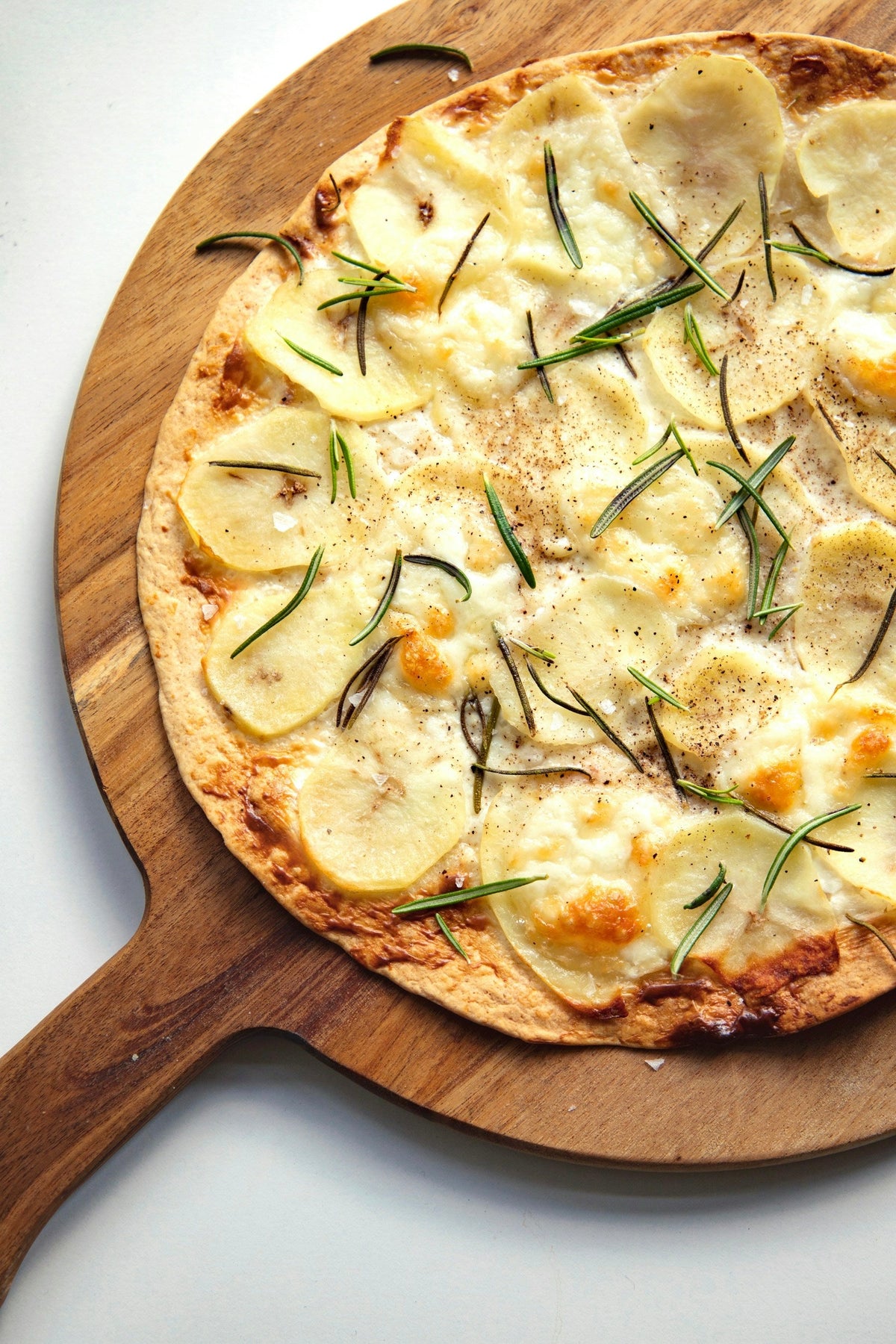 Stockfoto: Pizza Bianca mit dünnen Kartoffelscheiben, geschmolzenem Käse und Rosmarin. Foto: Josephine Amalie Paysen / Unsplash.