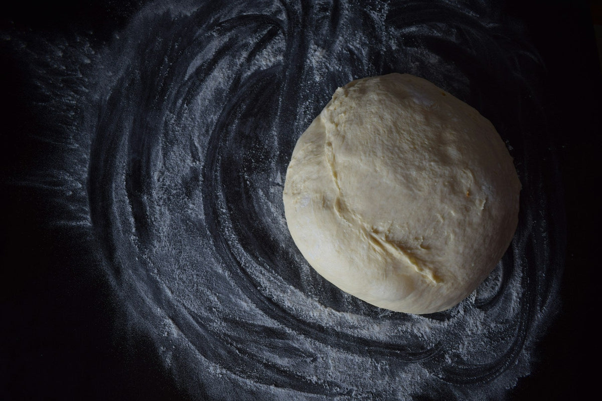 Stockfoto: runder roher Teigball auf einer mit Mehl bestäubten dunklen Arbeitsfläche. Foto: Tamara Gak / Unsplash.