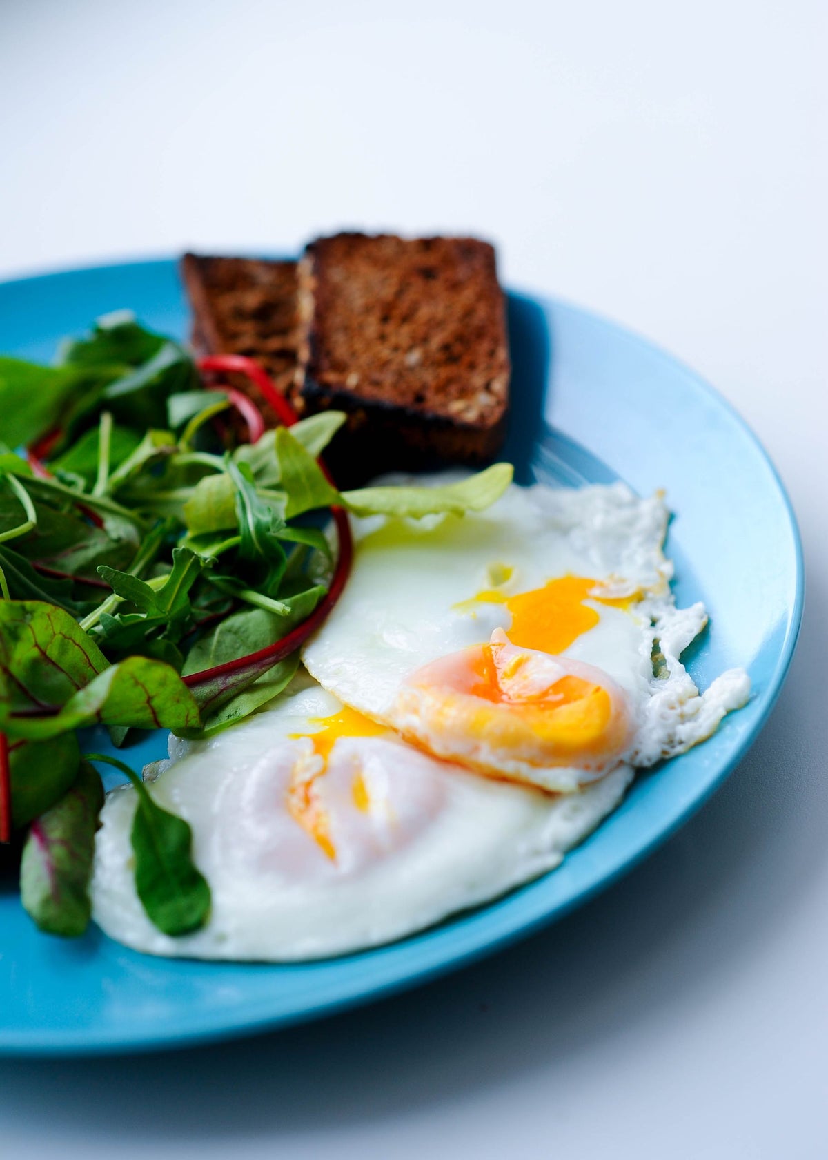 Stockfoto: Spiegeleier mit geröstetem Brot und Blattsalat auf einem Teller. Foto: Daka / Pexels.