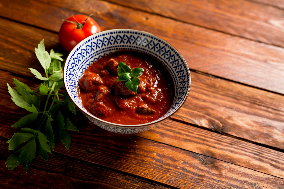 Servieridee: Gulasch mit Fleischstücken in roter Sauce in einer gemusterten Schale auf einem Holztisch. Foto: Michael Uebler / Unsplash.