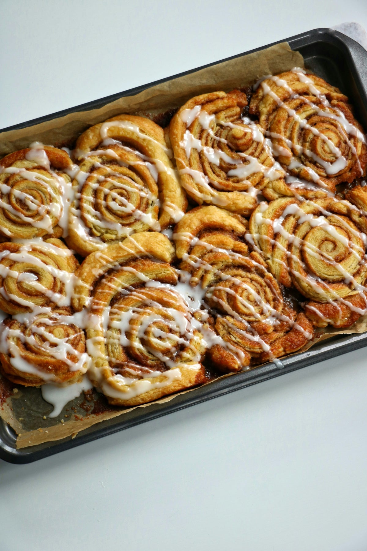 Servieridee: Gebackene Zimtschnecken mit heller Glasur auf einem dunklen Backblech. Foto: Anisa Cakesandbakes / Unsplash.