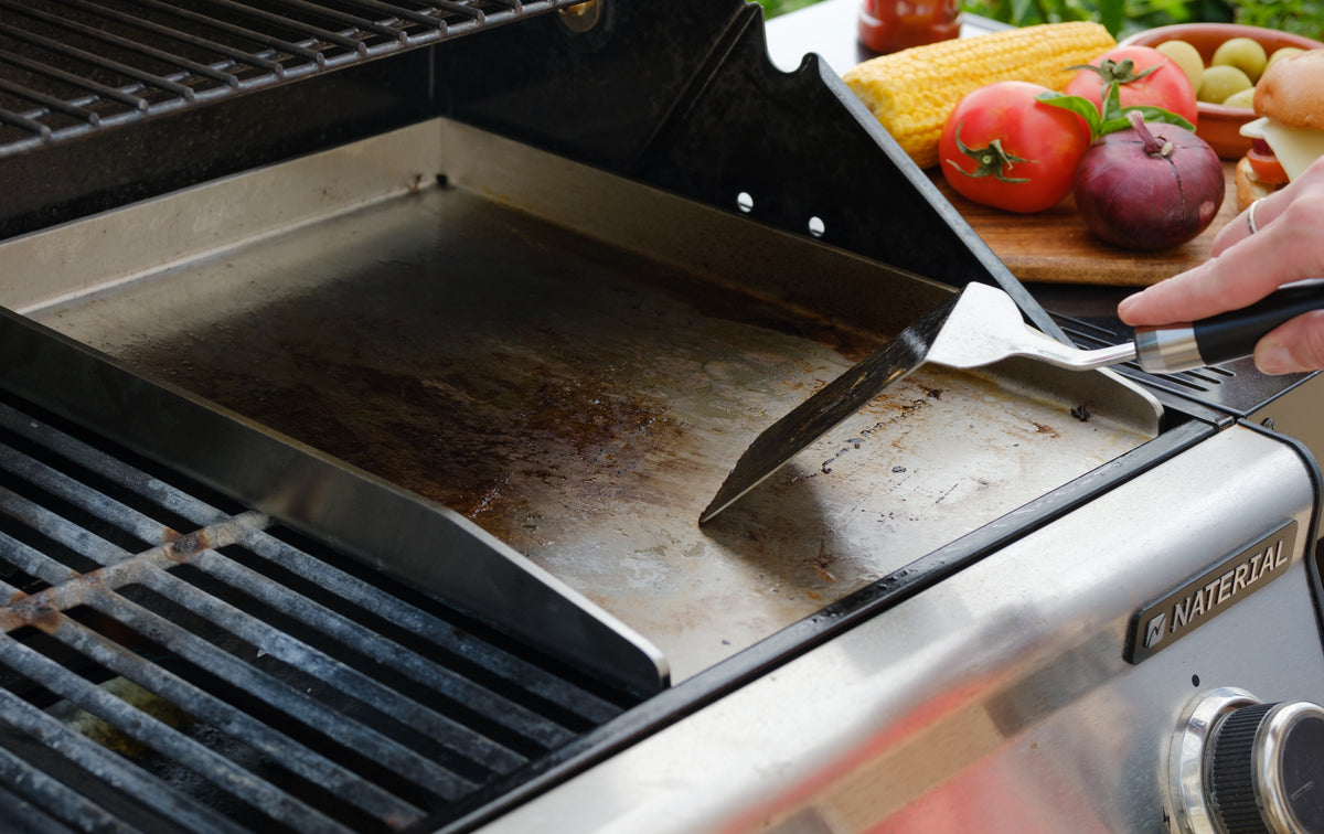 Edelstahlplancha mit Spachtel neben einem dunklen Grillrost